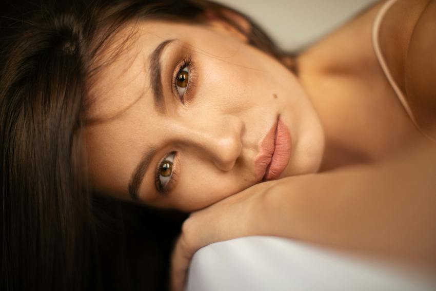 Gorgeous woman lays on edge of bed stairing into lense