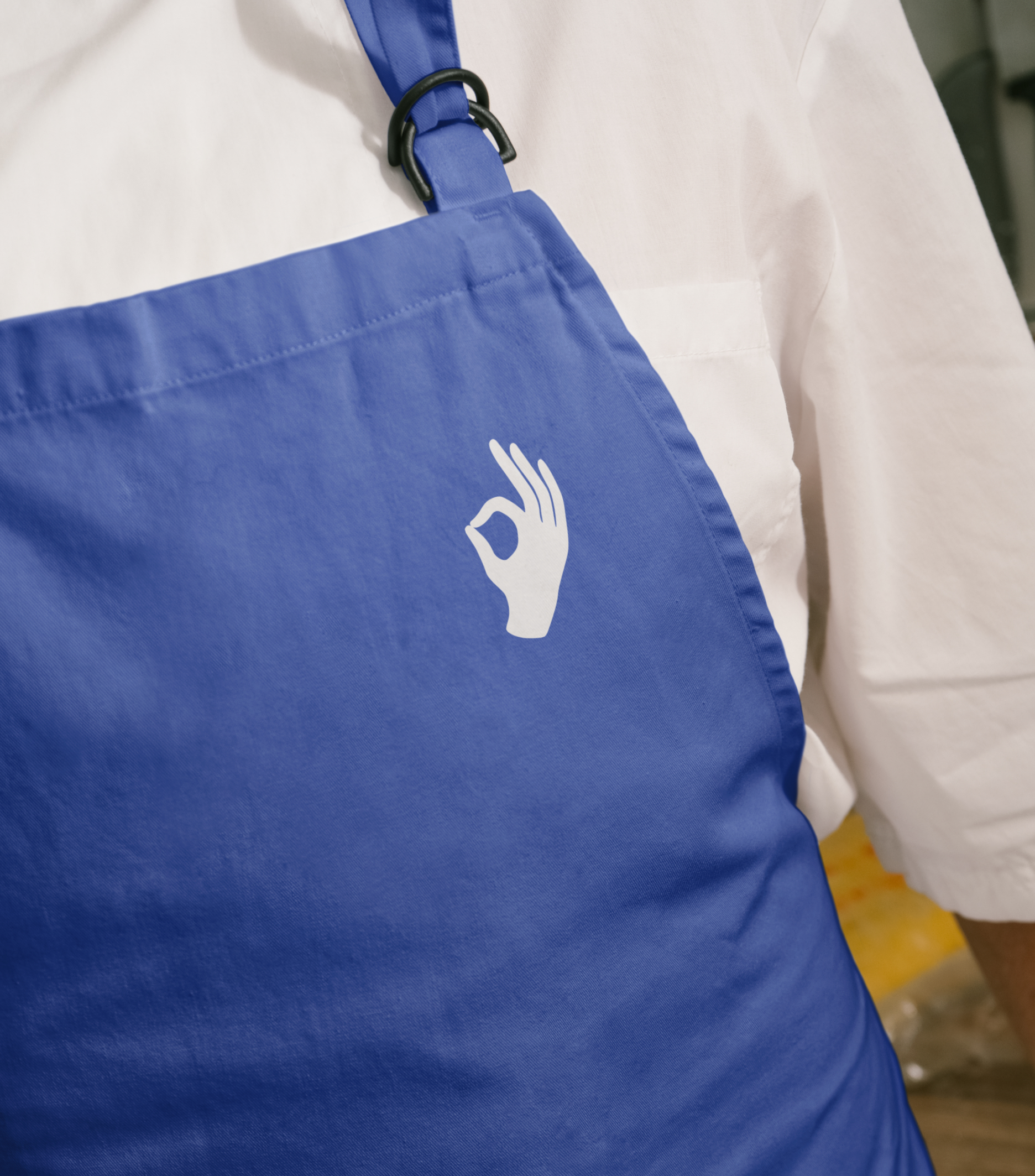 Close-up of a person wearing a blue apron with a white hand making an OK gesture printed on the chest.