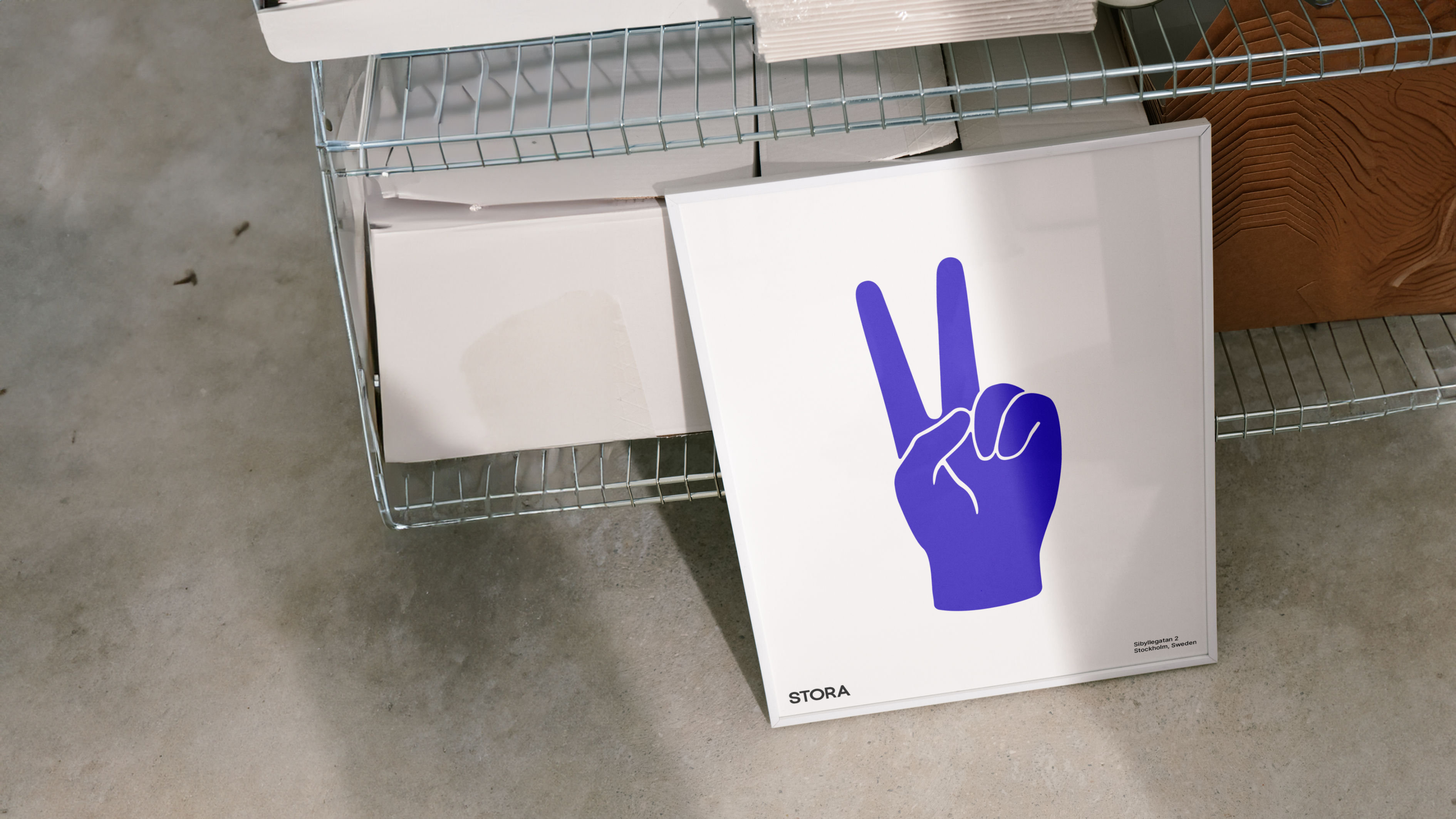 A white-framed poster showing a purple hand making a peace sign leans against a shelf filled with packaging materials.