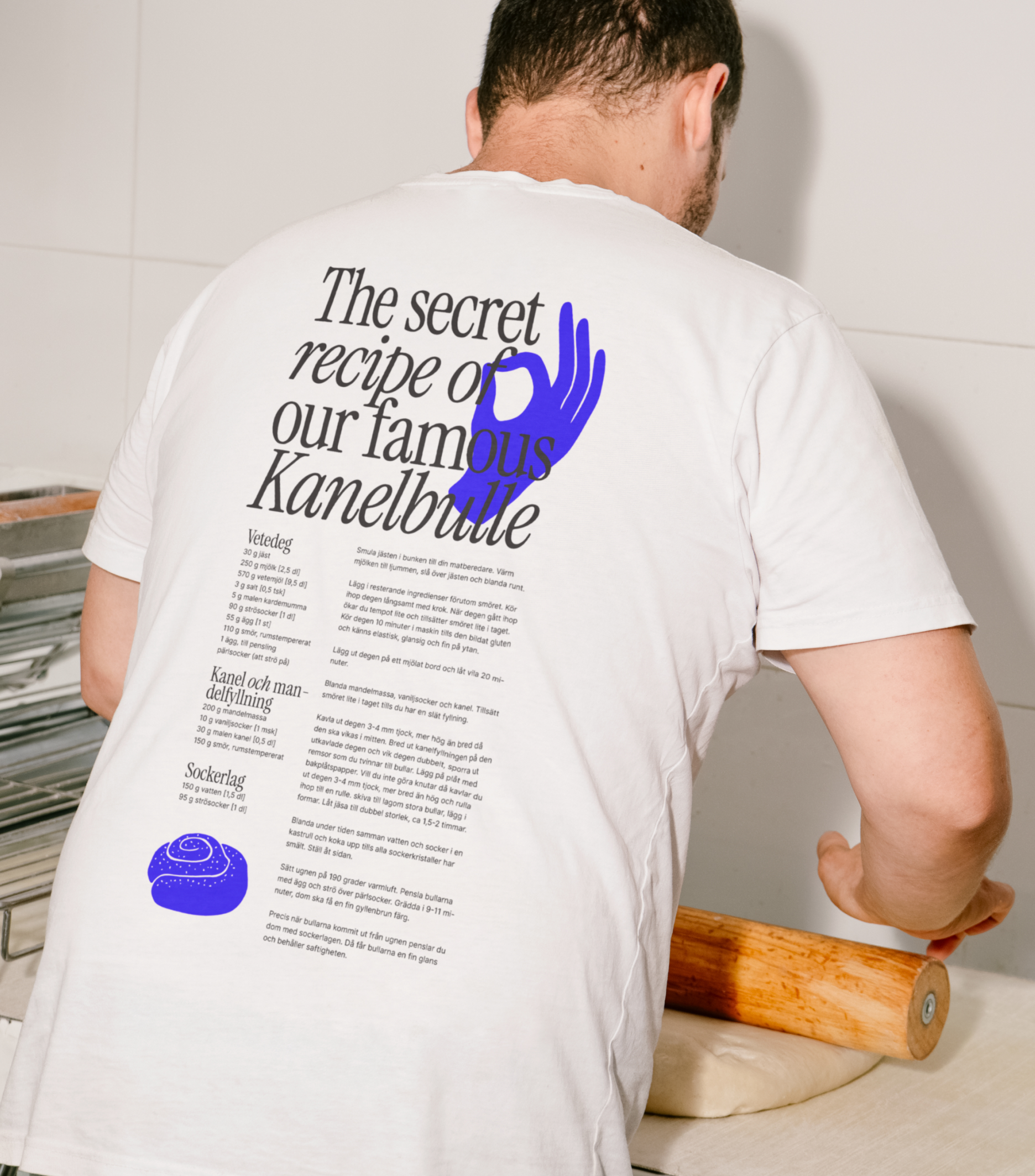 A person rolling dough wears a white t-shirt printed with a recipe for cinnamon buns and a blue OK hand symbol.