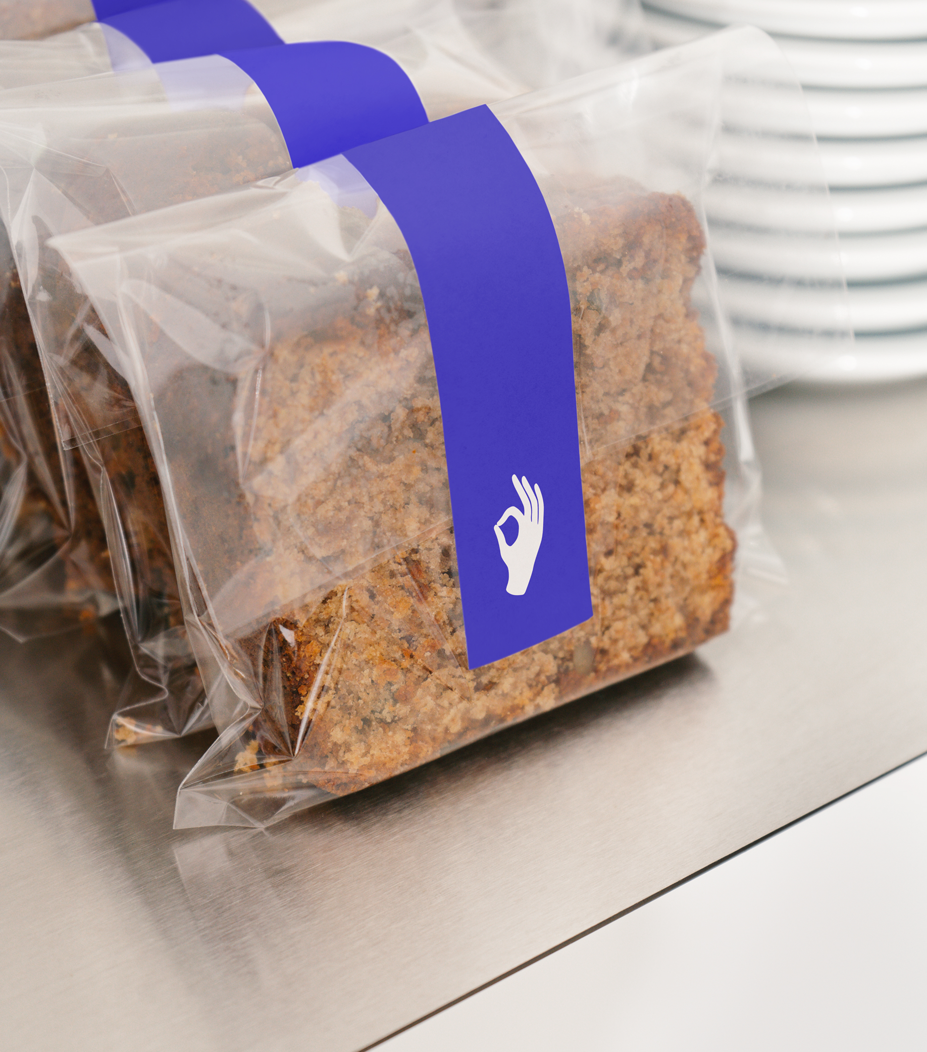 Slices of seed crispbread are sealed in transparent bags with purple labels featuring a white OK hand symbol.