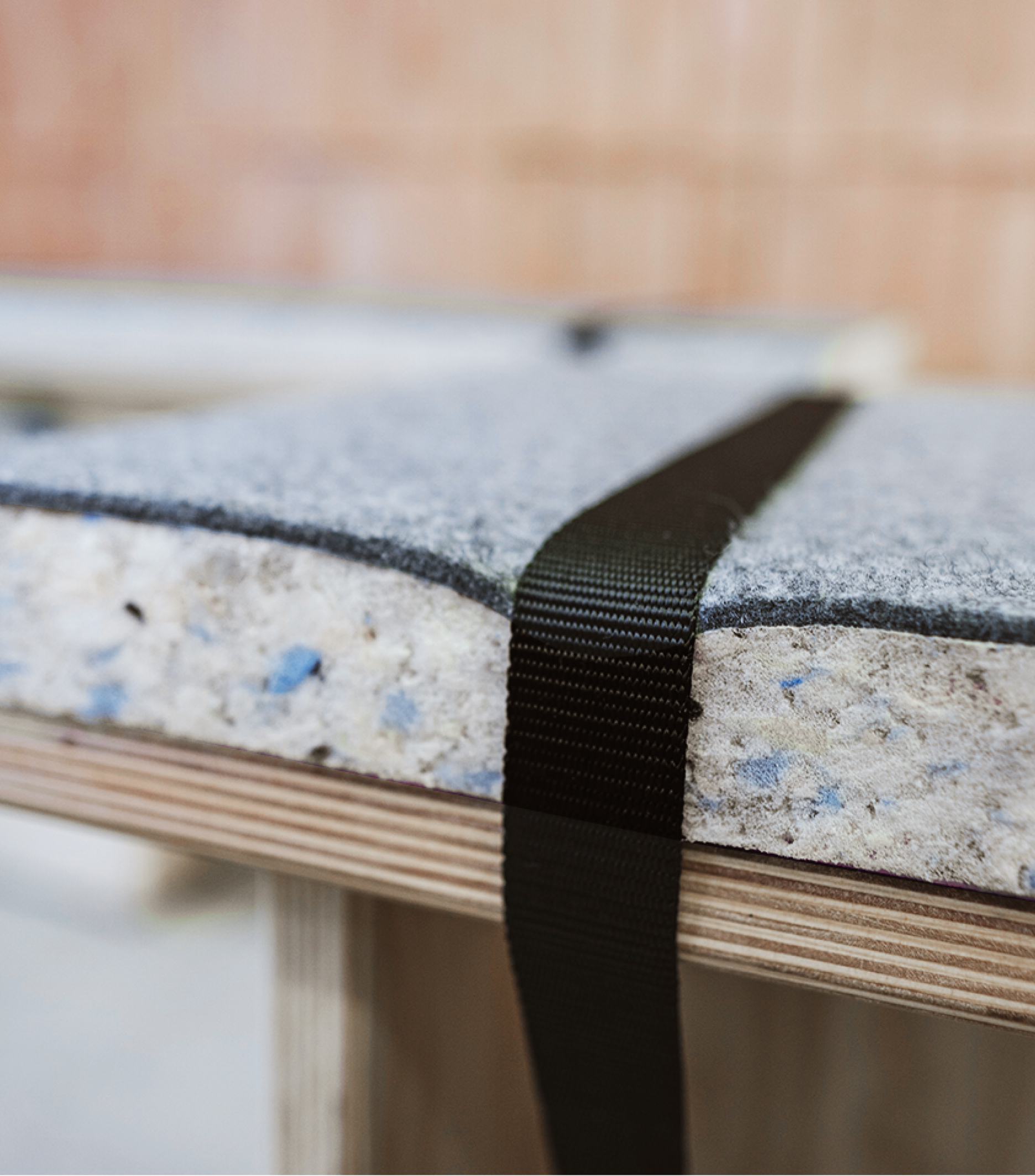 A detailed view of a recycled bench cushion with a black strap securing it to the wooden seat underneath.