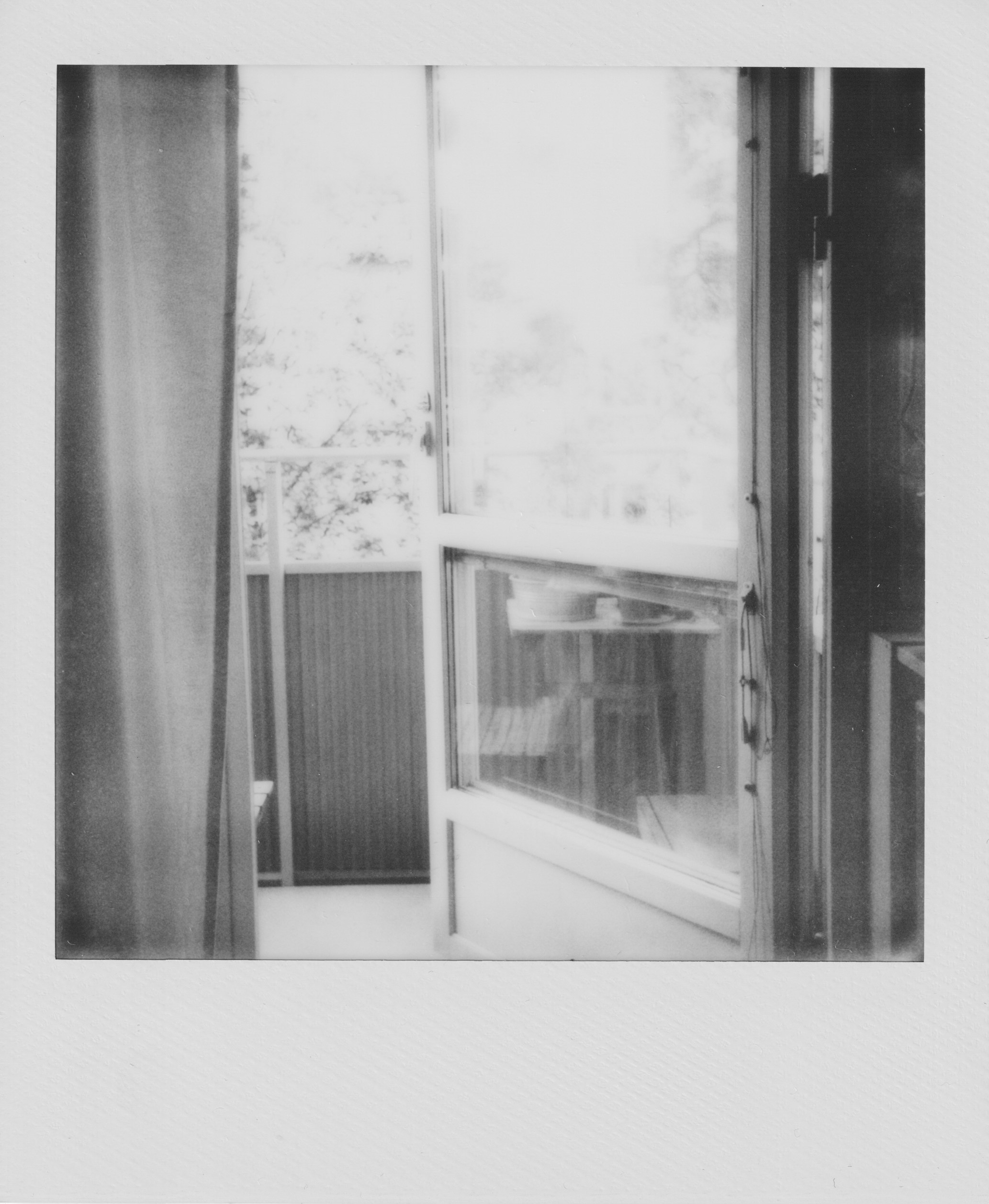 A scanned black and white Polaroid photograph, depicting an open balcony door.