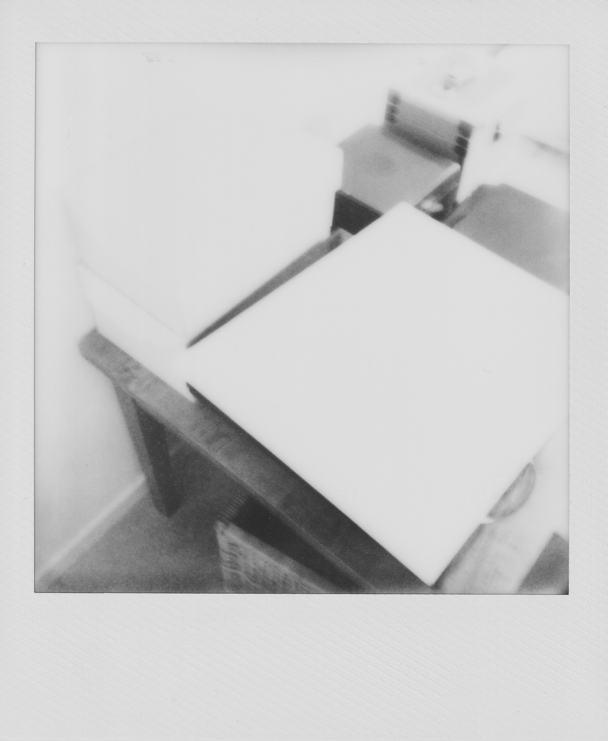 A scanned Polaroid photograph, semi-blurry, that depicts a table with some boxes of different shapes and colors on it.