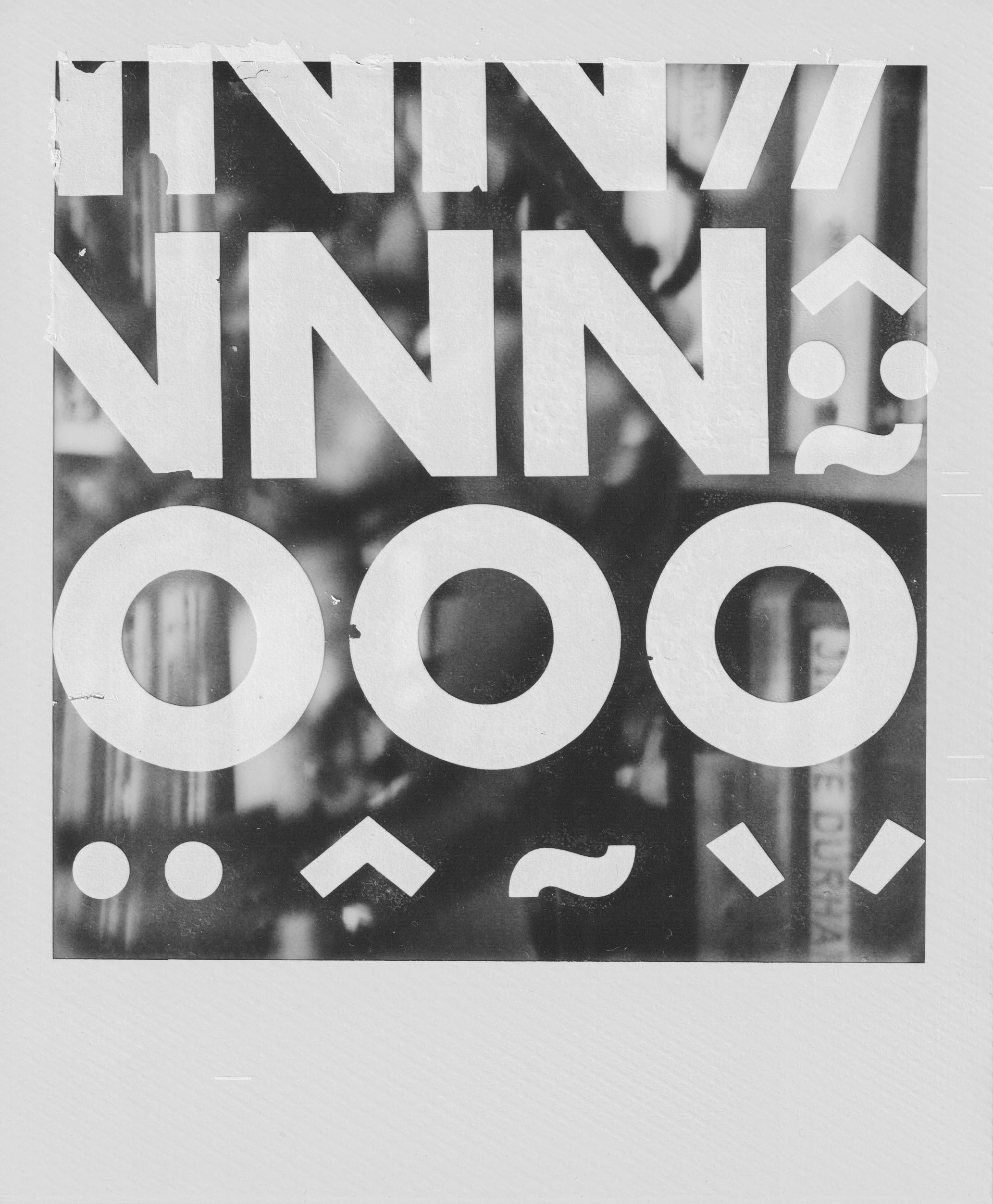 A black-and-white Polaroid photograph and abstract collage. The background is a blurred interior - faint outlines of bookshelves and indistinct books. Printed on top is a translucent overlay covered in rows of bold, white Helvetica characters: a top row of three large “N” shapes, a middle row of three large “O” circles, and a bottom row of punctuation marks - two dots, a caret, a tilde, and two angled accents - arranged in a tight, rhythmic grid. The characters were applied using outdated Letraset transfers, a dry-transfer system graphic designers used before computers.