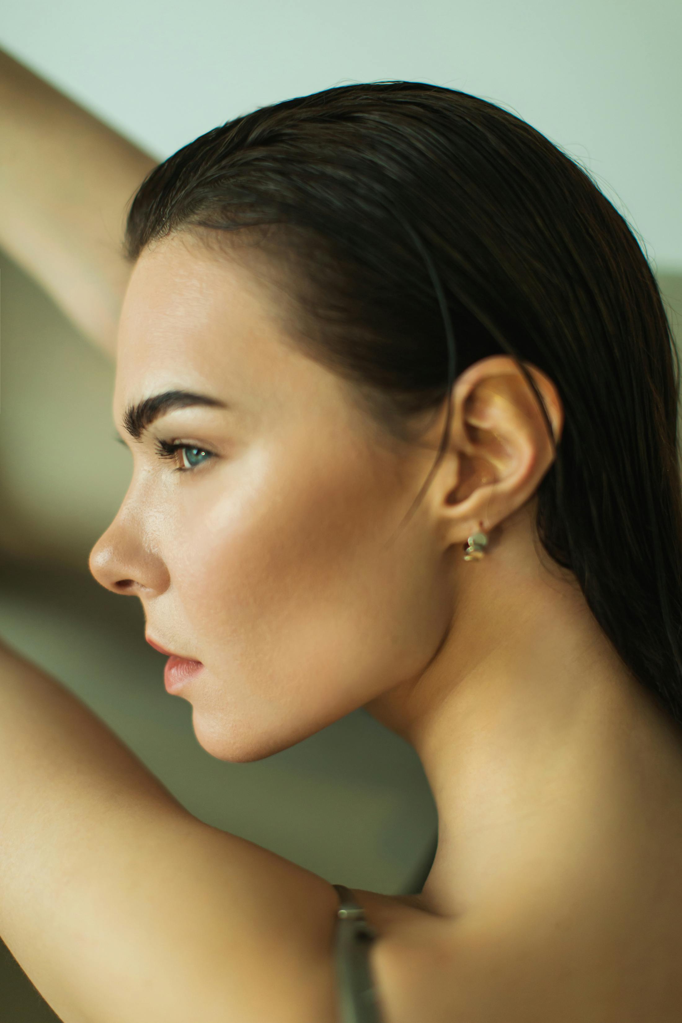 A younger woman with great eyebrows is facing away from the camera with her head turned to the left. Her hair is slicked back and she has minimal makeup