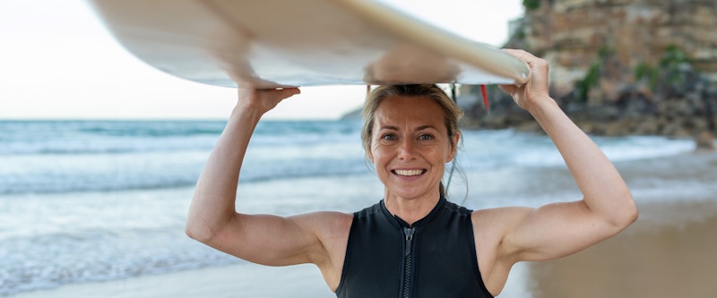 Woman on the beach holding a surfboard smiling