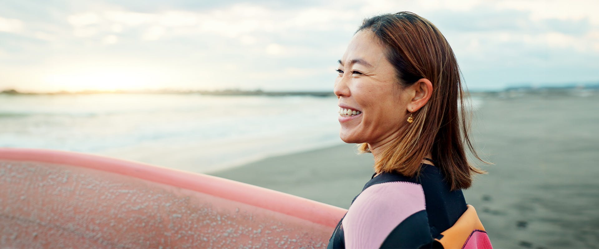 Woman holding a surf board at the beach smiling