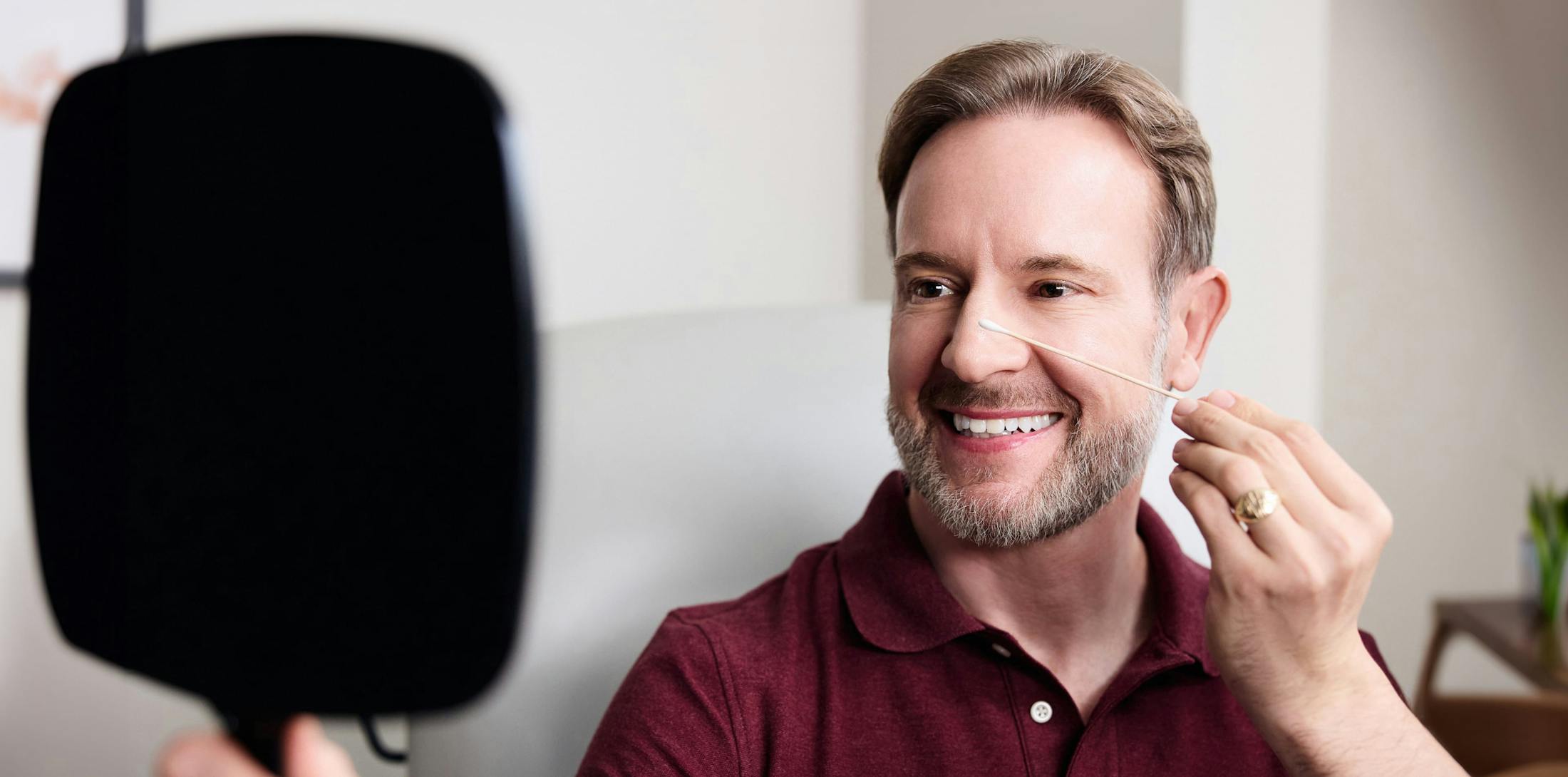 Man looking at himself in the mirror, holding a cotton swab