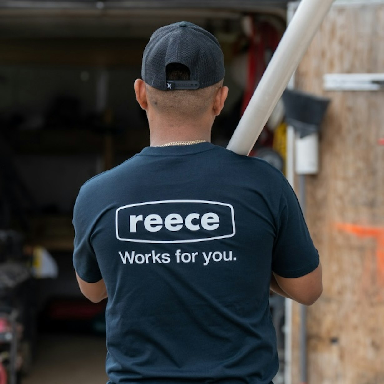 The back of someone in a Reece t-shirt carrying pipe