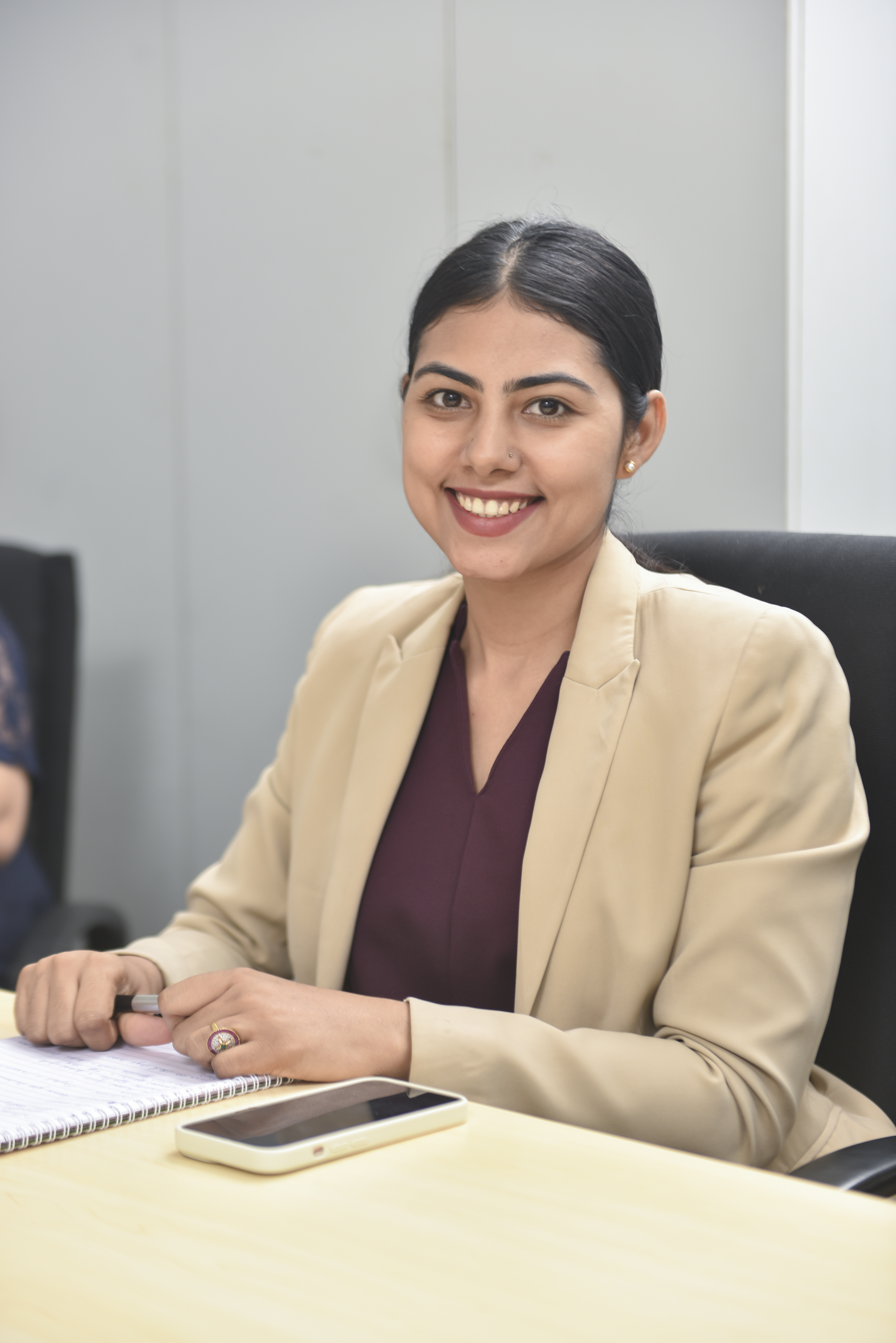 IN - woman in suit sitting at a desk smiling at camera