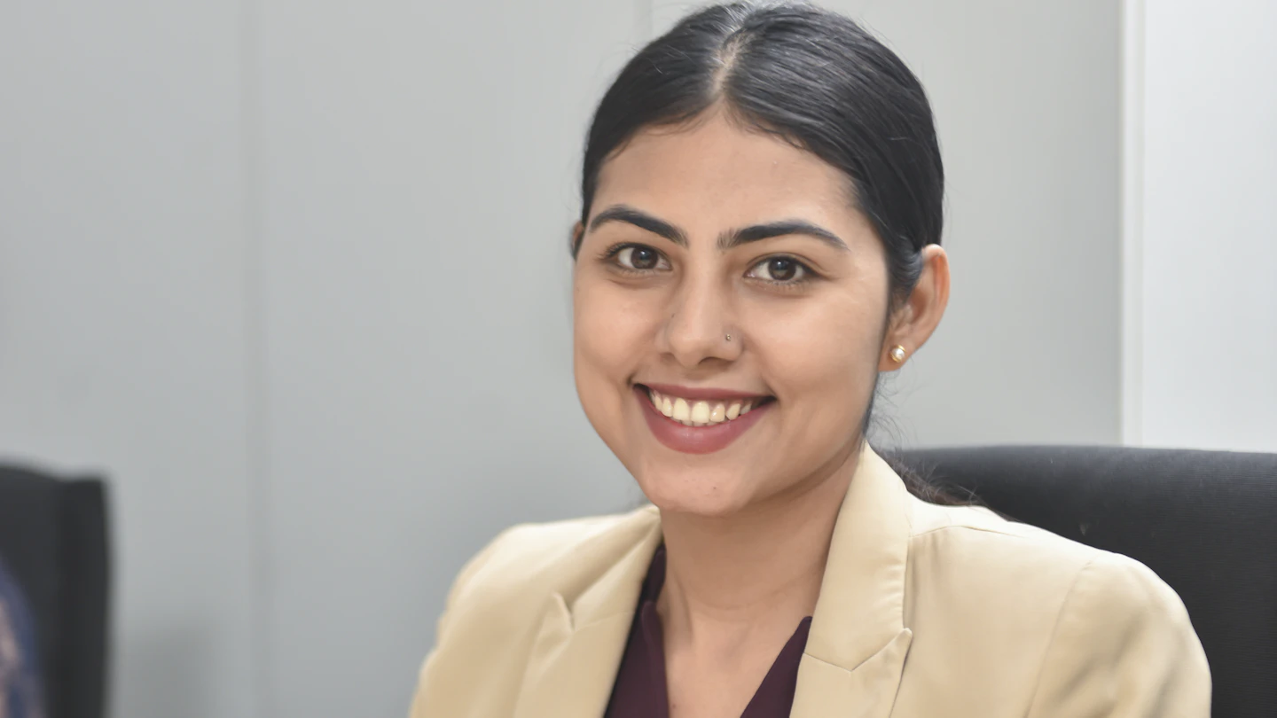 IN - woman in suit sitting at a desk smiling at camera