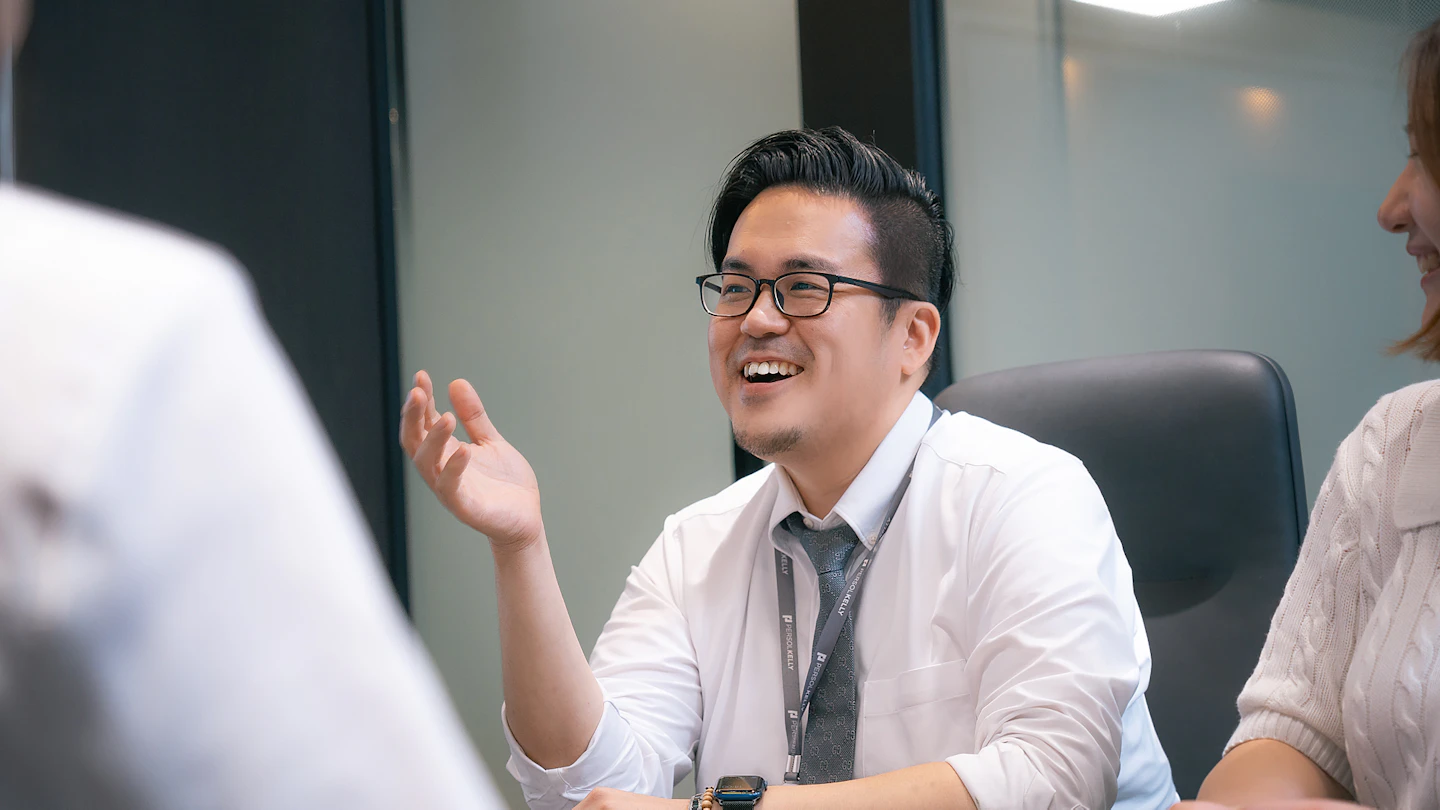KR - smiling man talking to colleagues across a desk
