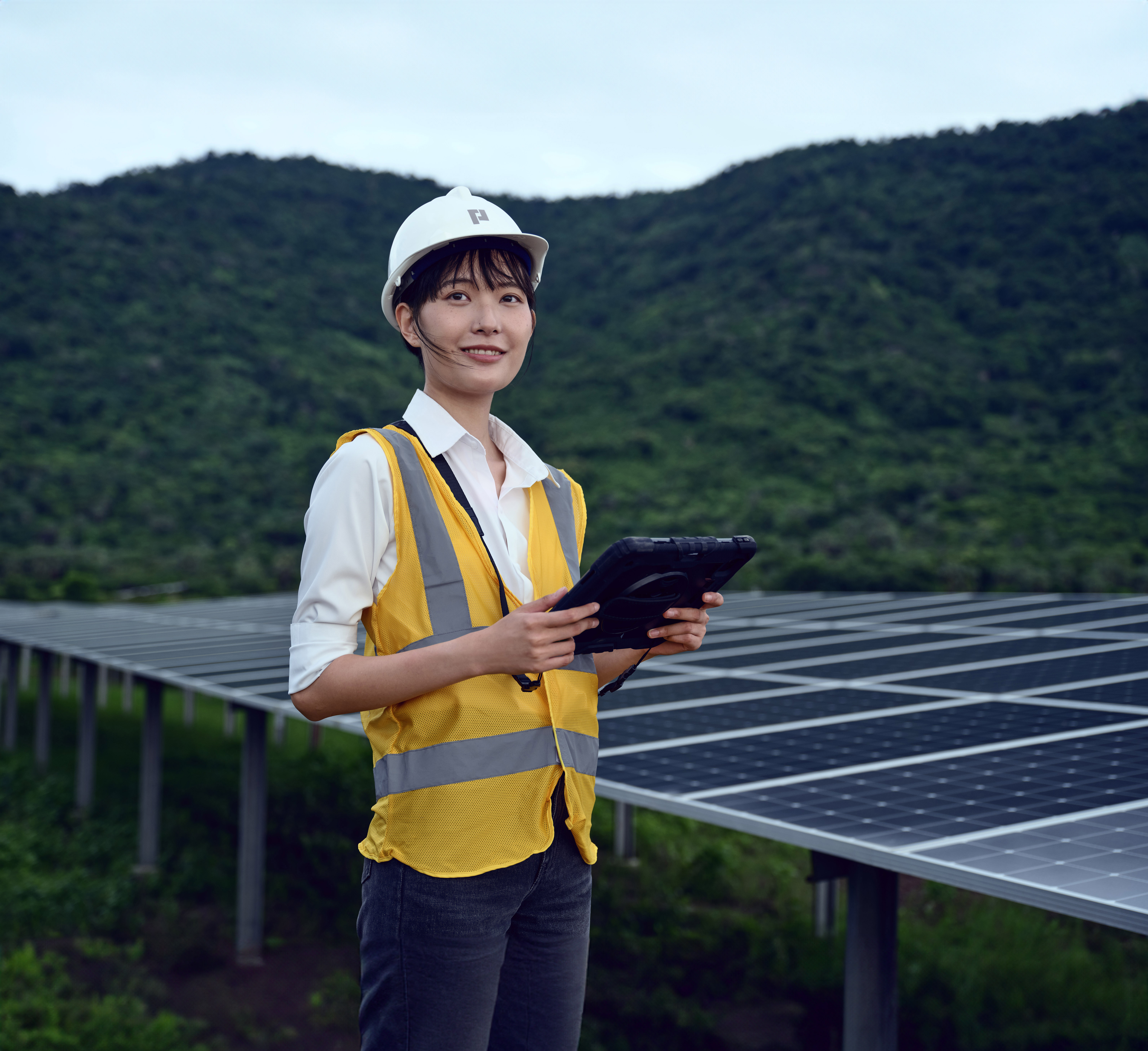 Contract worker in hi-vis vest and hard hat using a tablet at a solar farm