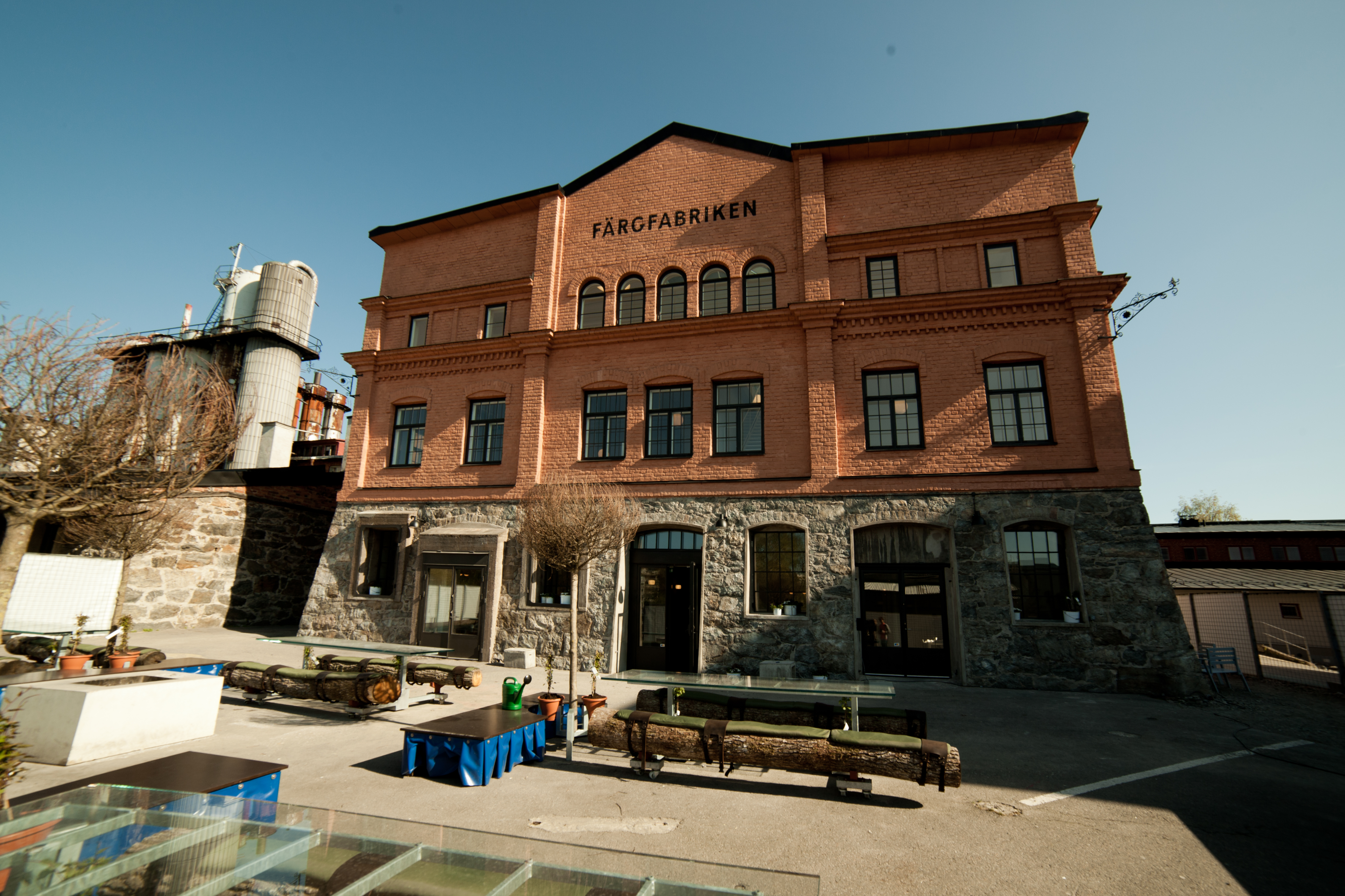 Röd byggnad i solljus, uteplats med långa bänkar.