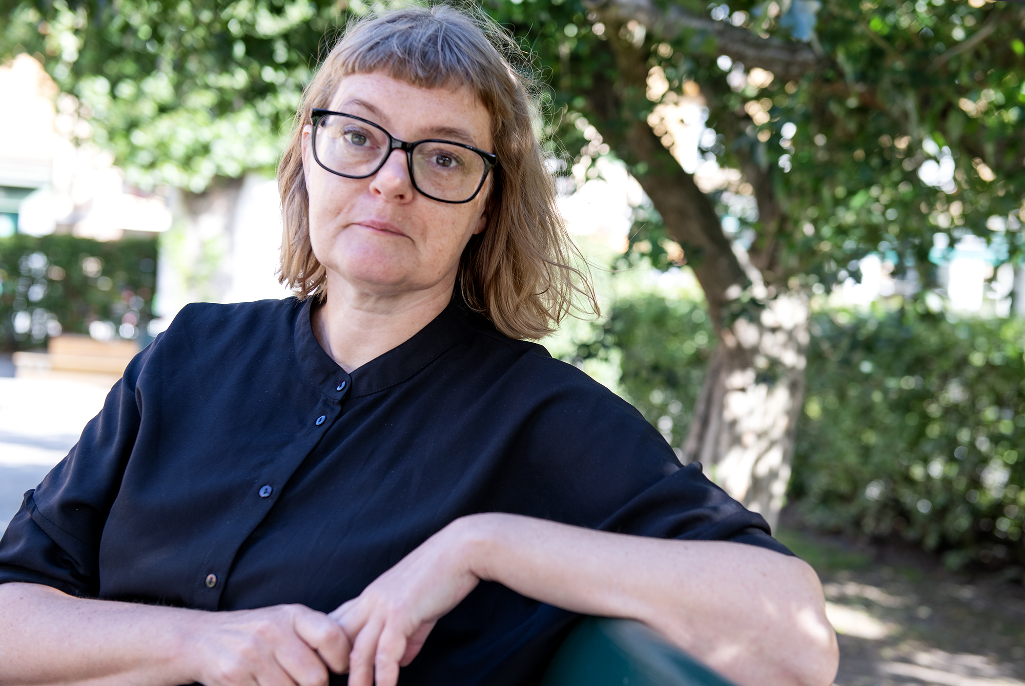 Amanda Creutzer  allvarlig på bänk i sommargrönska. Hon föreläser om upphandling inom projektet KnowHow