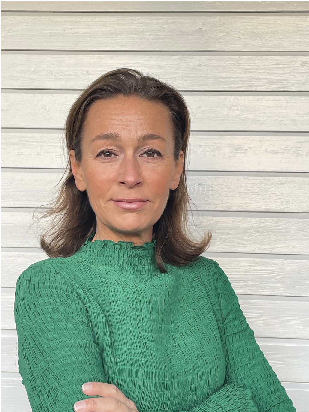 Cathrine Mellander Backman står självsäkert med armarna i kors. Brunt axellångt hår och grön topp