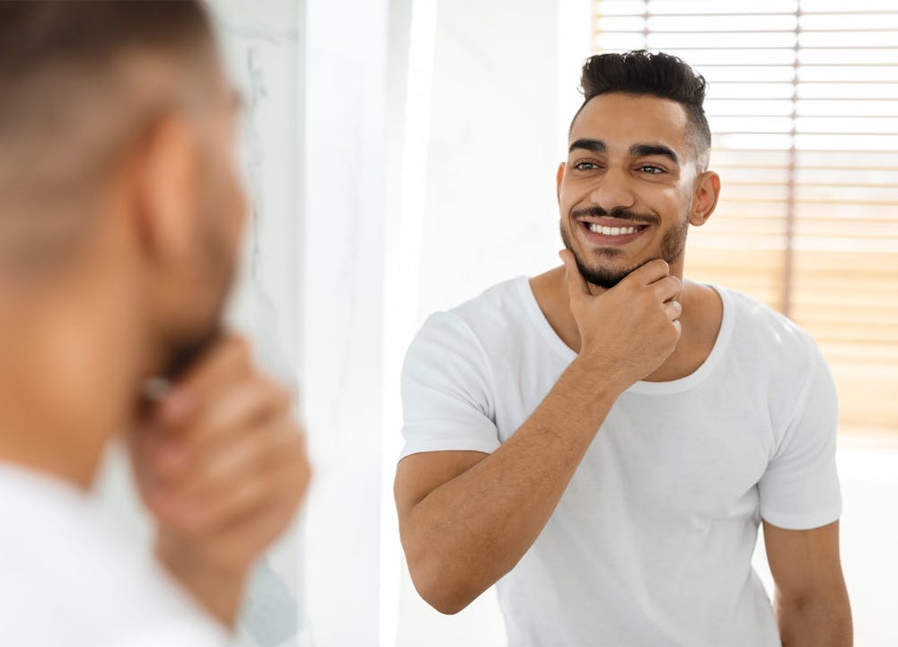 man looking in a mirror, smiling and touching his chin