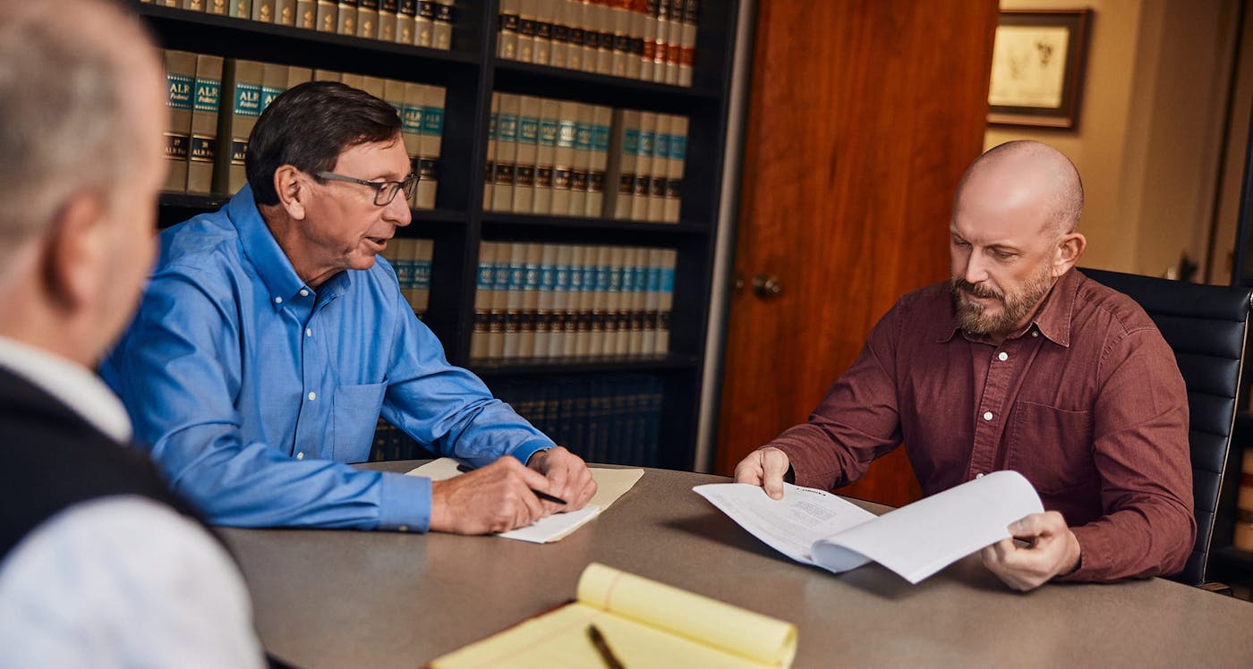 3 men sitting at table loooking at paper