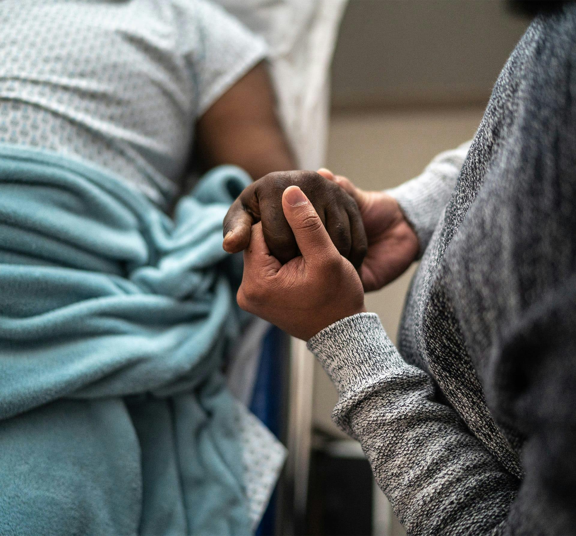 person holding someone's hand while they lay in a hospital bed