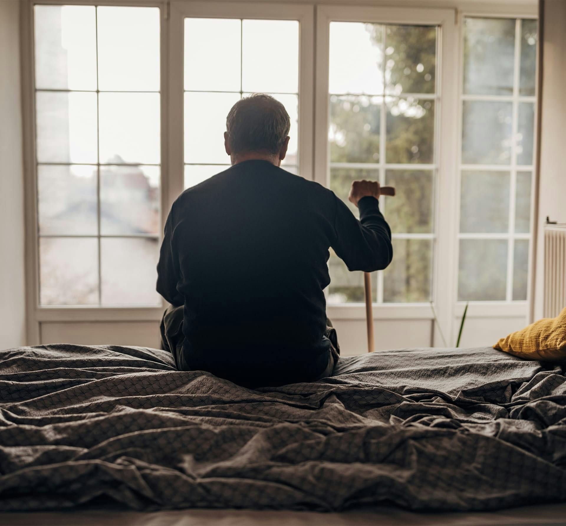 man with cane sitting on edge of bed