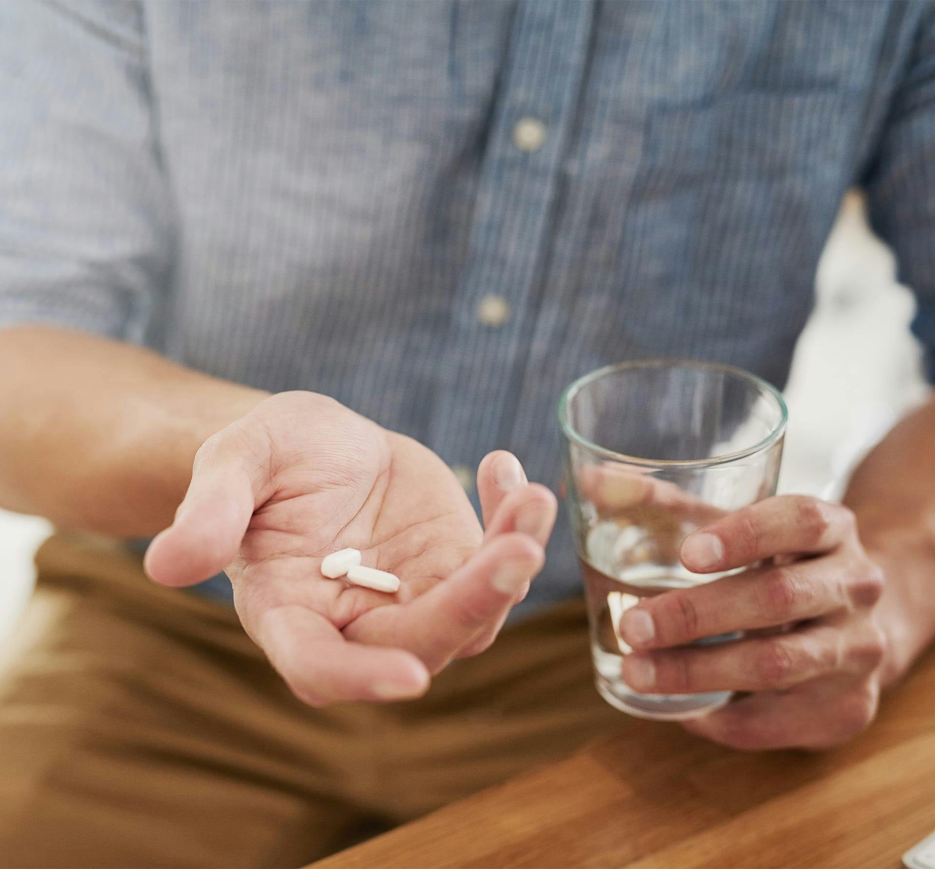 man holding glass of water and 2 pills