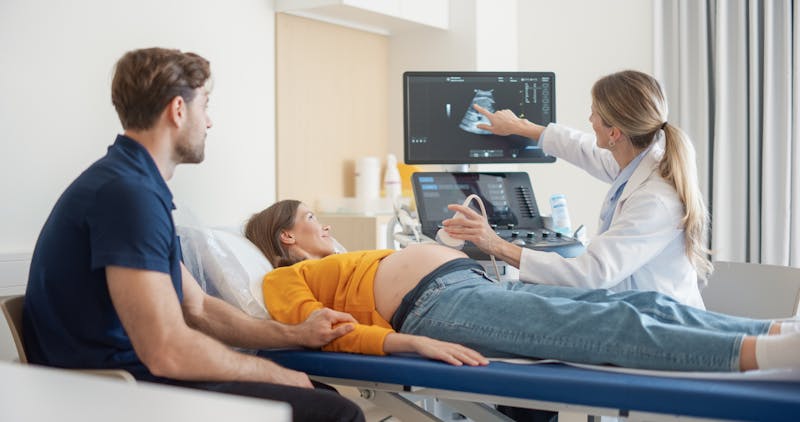 Pregnant woman undergoing an ultrasound examination while a doctor reviews the results with her partner present.