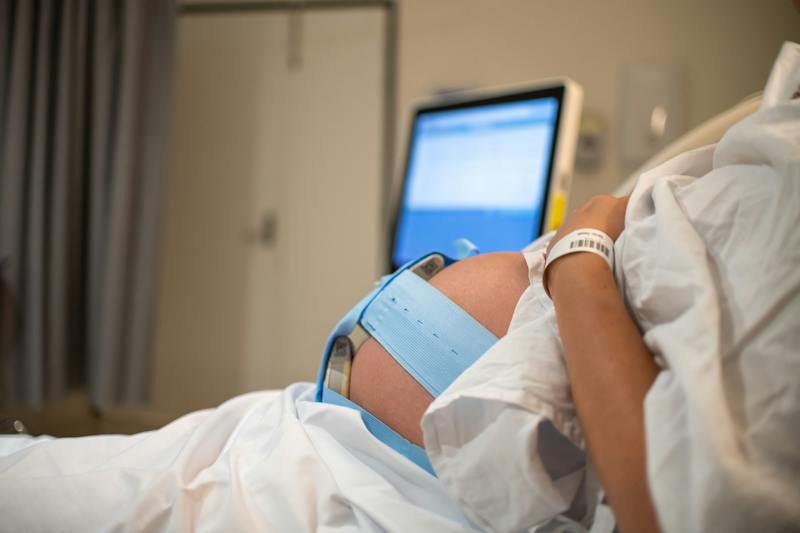 Pregnant patient wearing fetal monitoring belts during labor in a hospital.