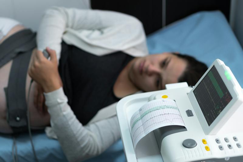 Pregnant patient undergoing fetal heart monitoring with fetal heart rate strips visible.
