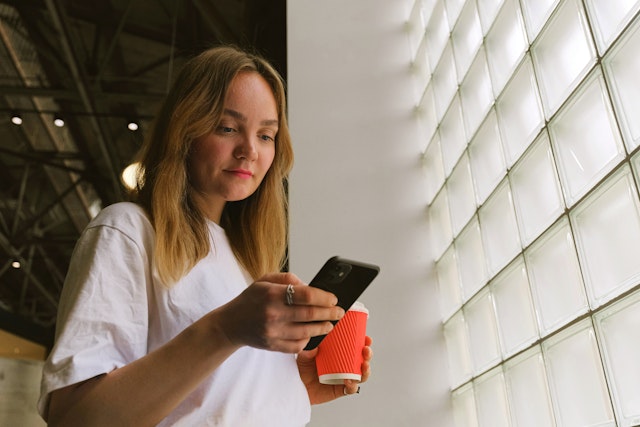 Donna che usa Satispay dallo smarphone, una tazza di caffé in mano