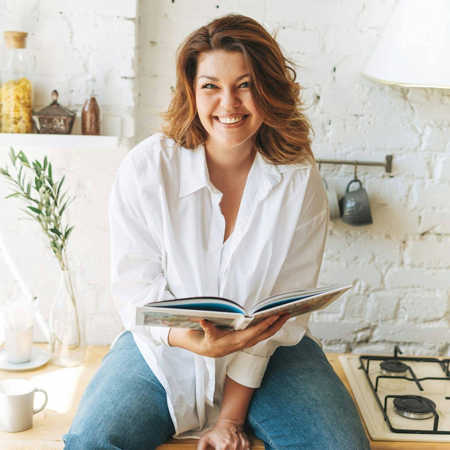 woman sitting on a kitchen counter, holding a book