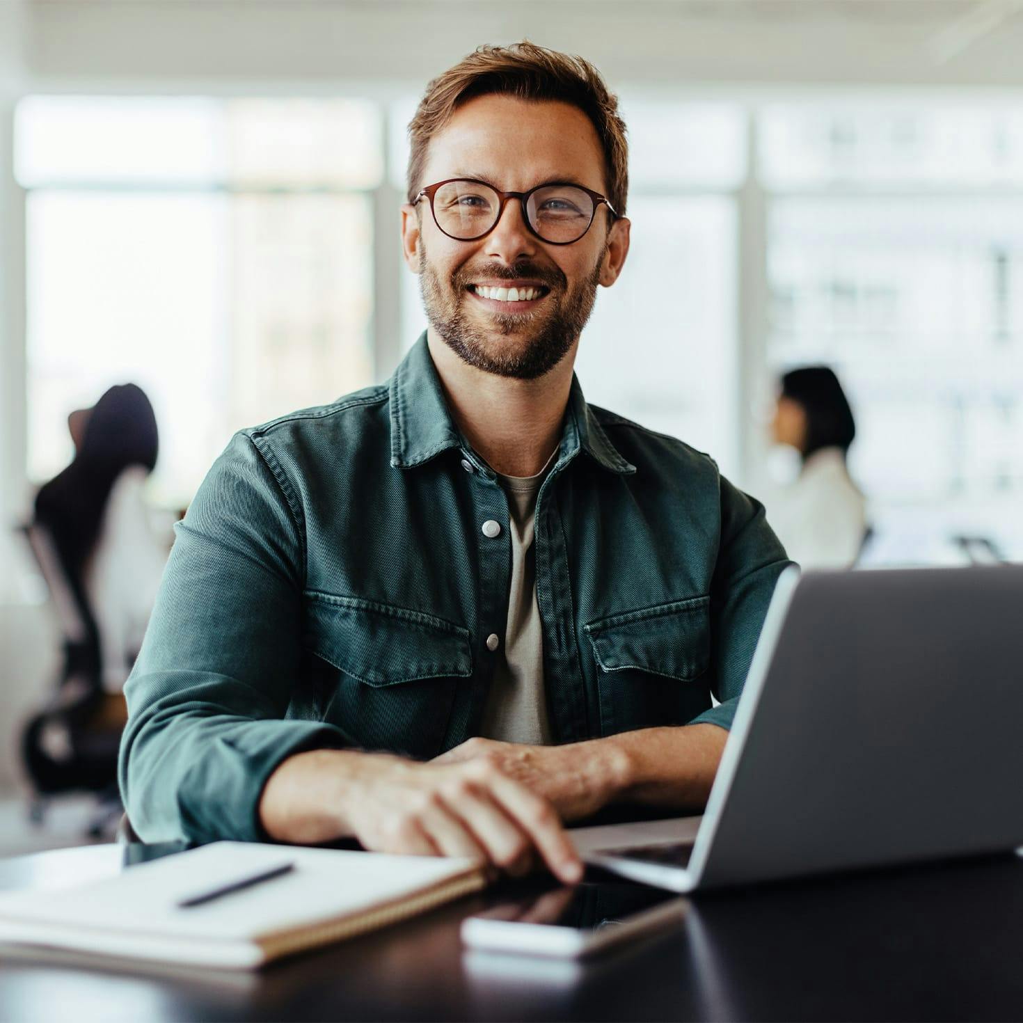 man smiling, sitting at a table with a laptop