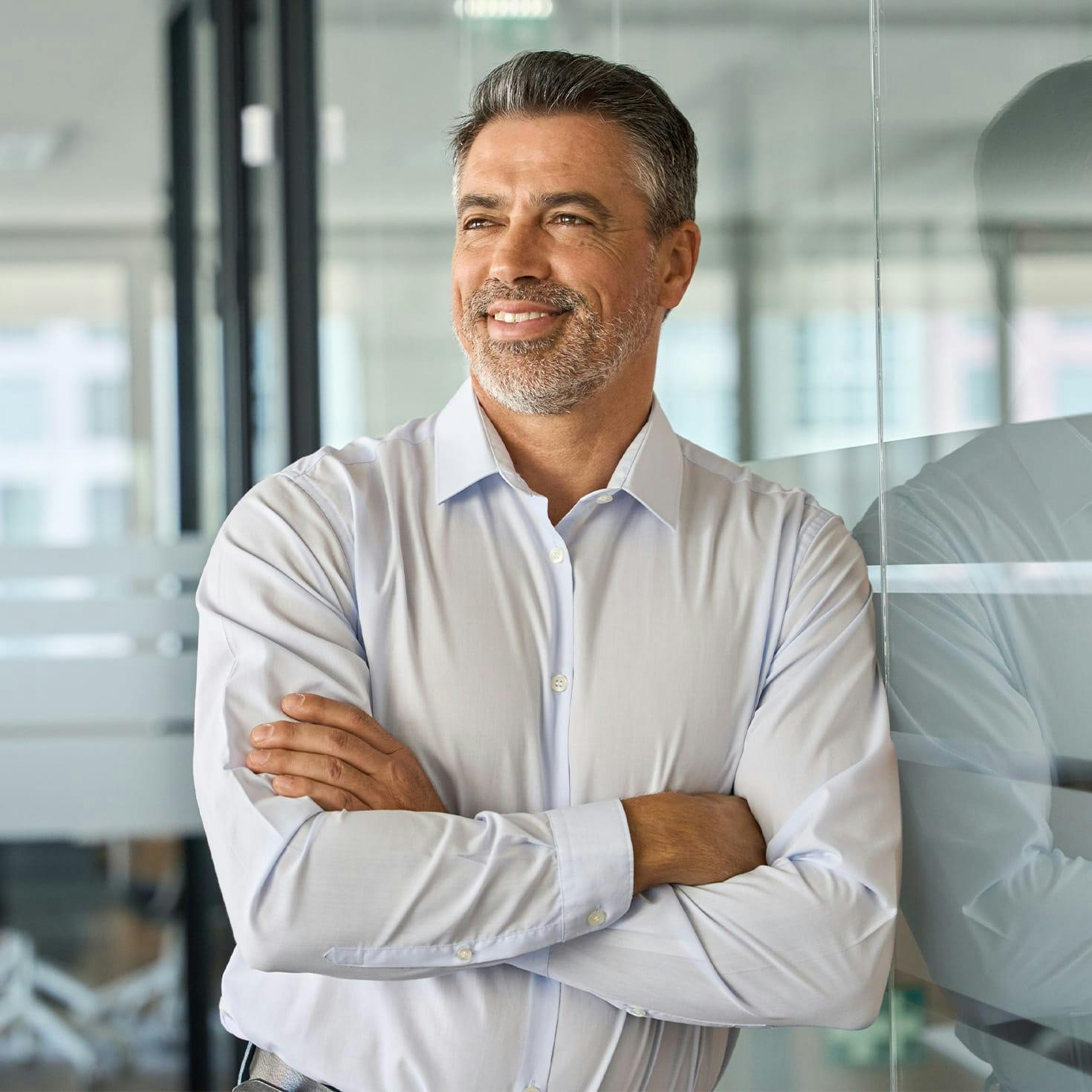 man crossing his arms, leaning against a glass wall
