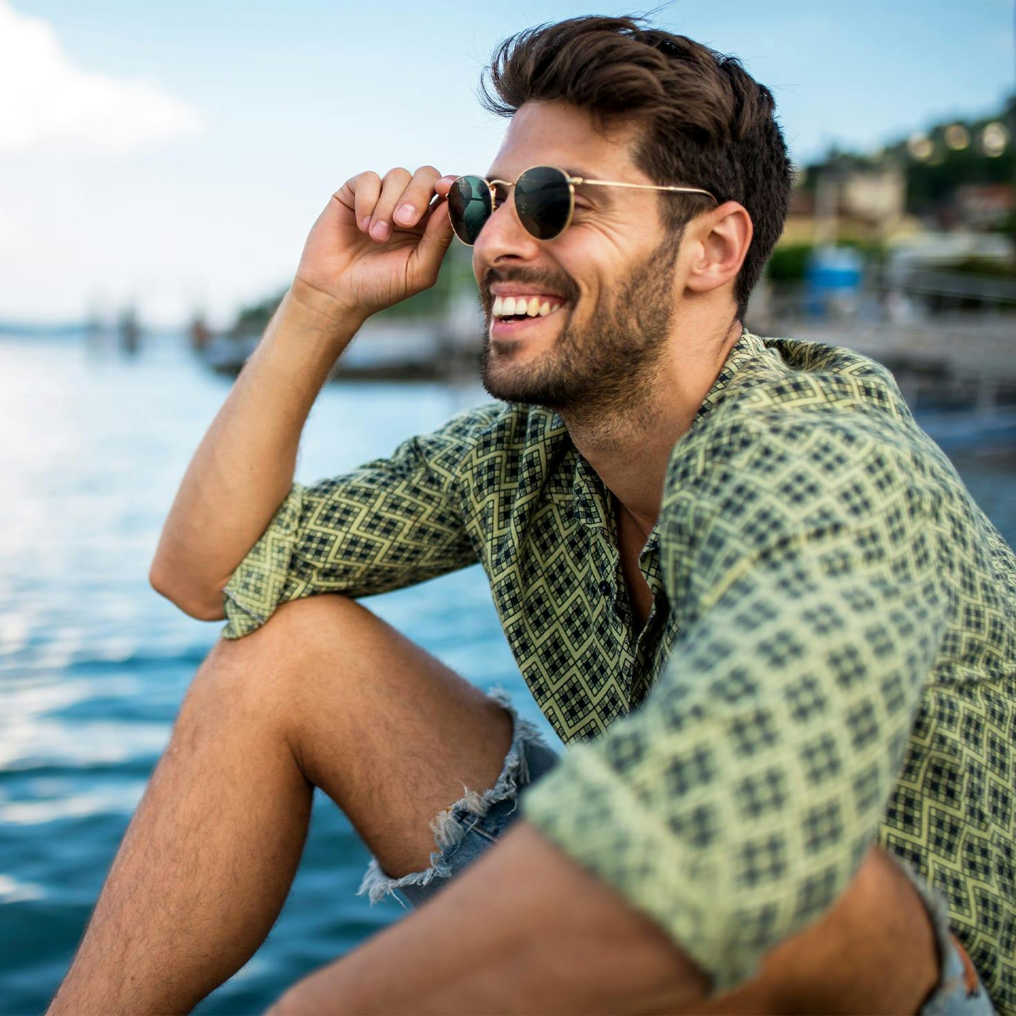 smiling man sitting on a beach, holding his glasses