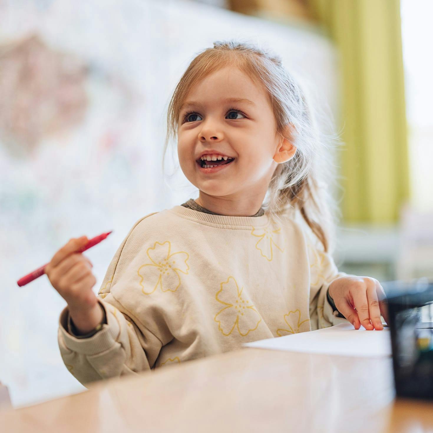 young girl smiling, holding a colored pencil