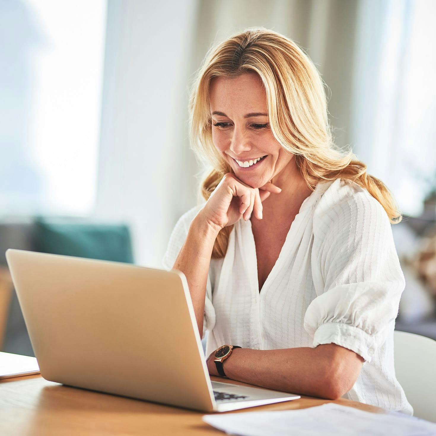 smiling woman resting her head on her hand, looking at a laptop