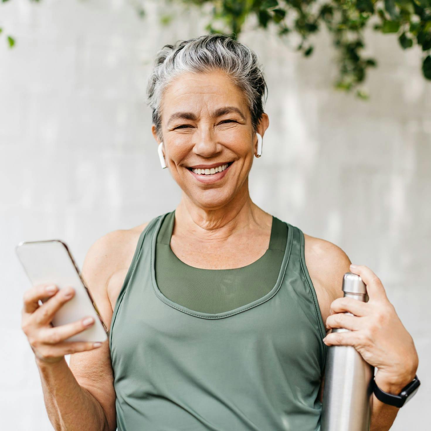 older woman smiling, holding a phone and a water bottle