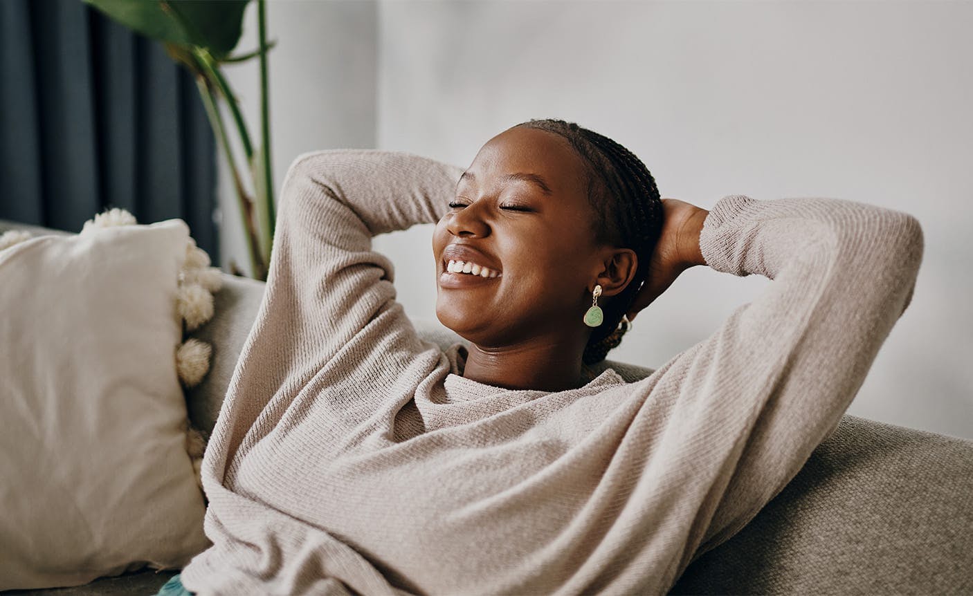 woman sitting on a couch, holding her hands behind her head