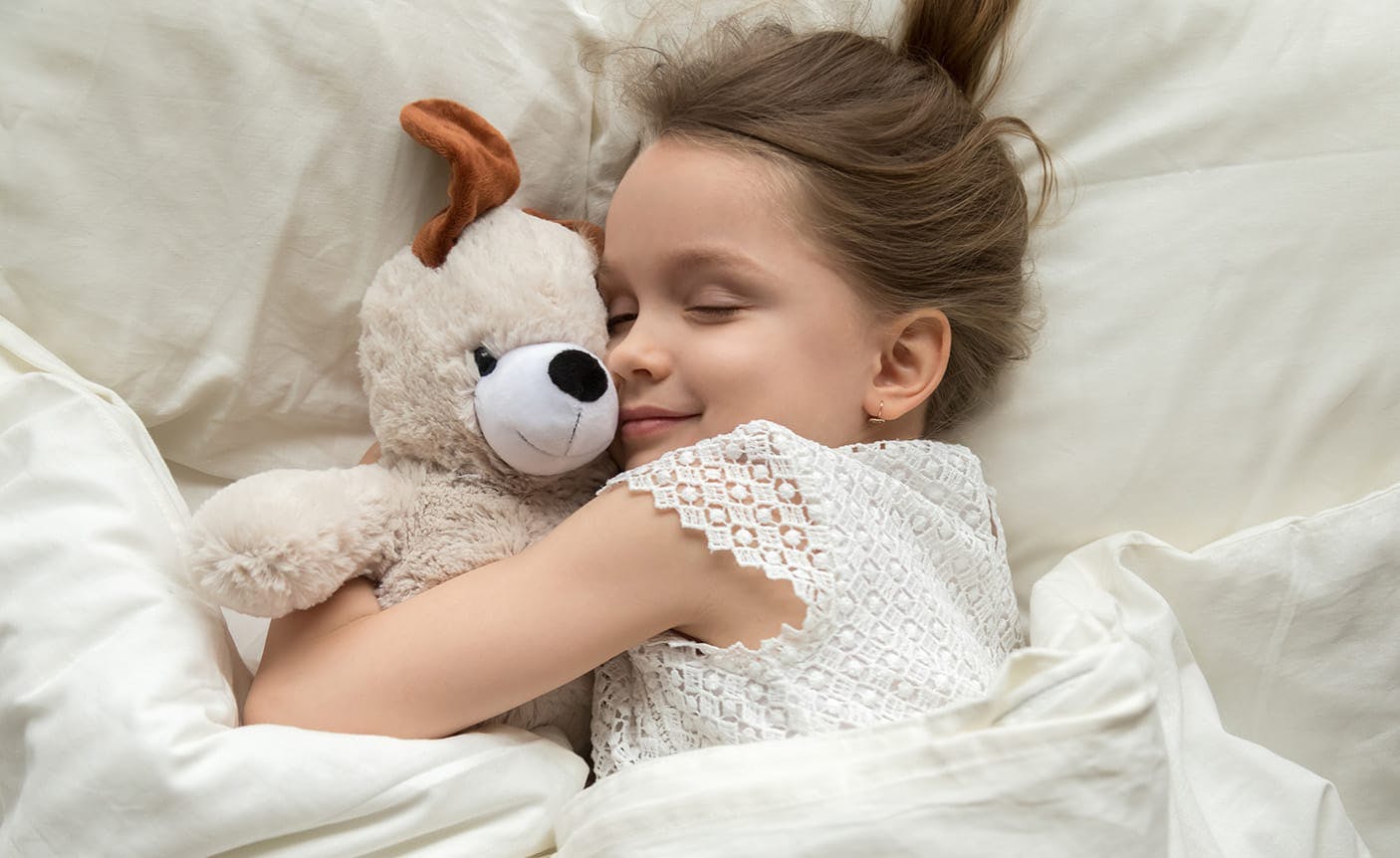 little girl snuggling a stuffed dog in a bed