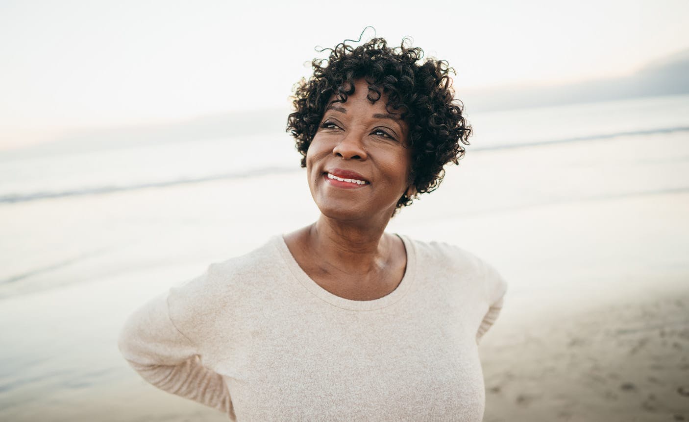 older woman smiling, standing on a beach