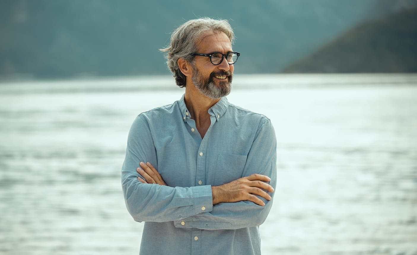 man standing in front of a lake, crossing his arms