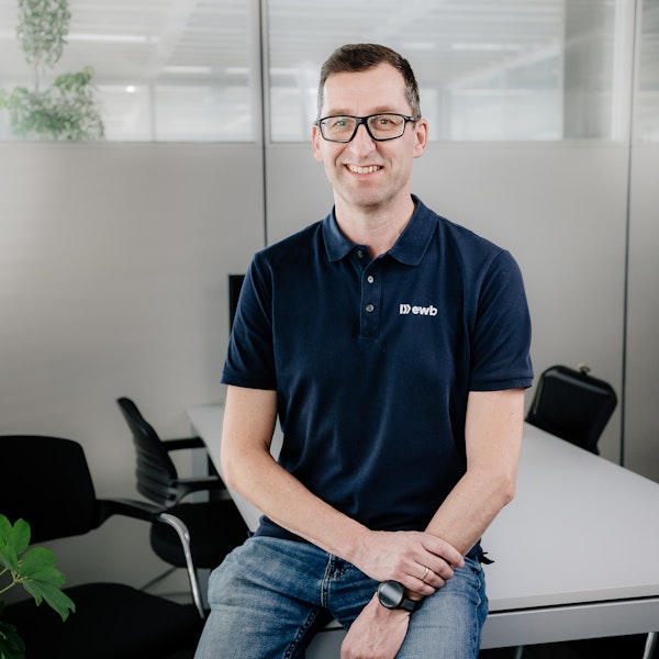 Johann Köck sitzt an seinem Arbeitsplatz und lächelt in die Kamera.