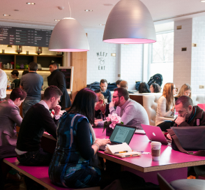 Diverse group of people sitting in an office cafe eating, drinking and working
