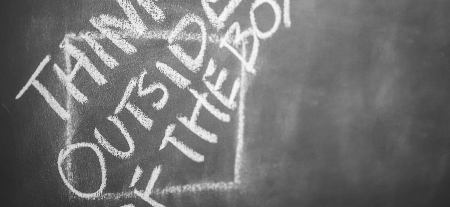 Photo of a chalkboard with a chalk drawing of a box and the text "Think outside of the box"