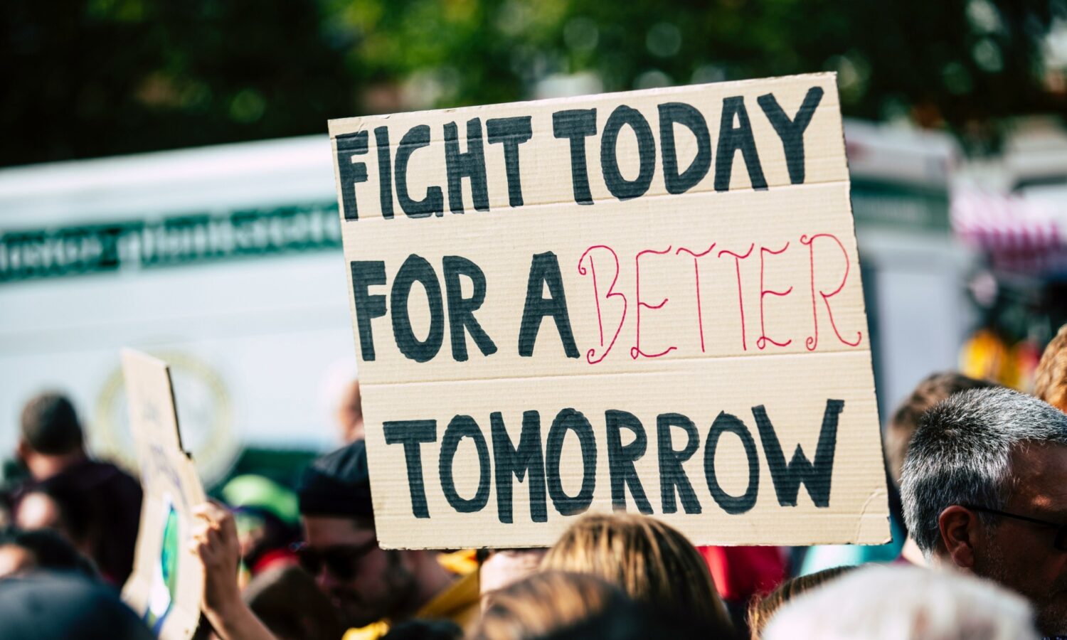 A demonstrator holds a cardboard sign reading "Fight today for a better tomorrow."