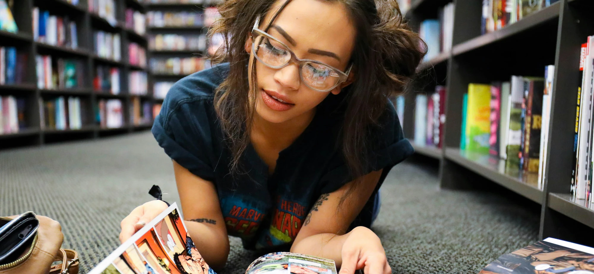 Tattooed girl reading comic books in a library Photo by Joe Ciciarelli on Unsplash
