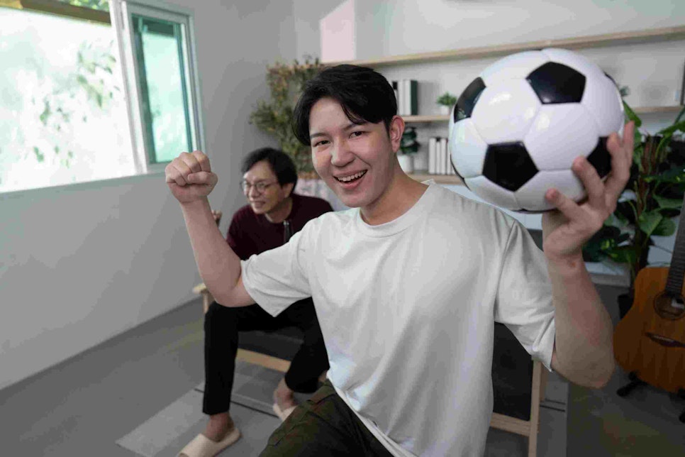 Excited son celebrating soccer victory with father in living room