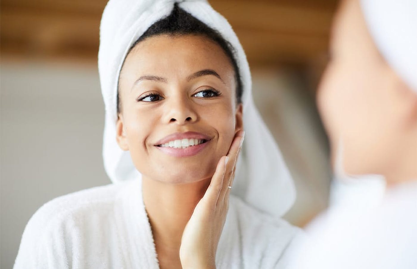 woman with robe and hair in towel touching her face