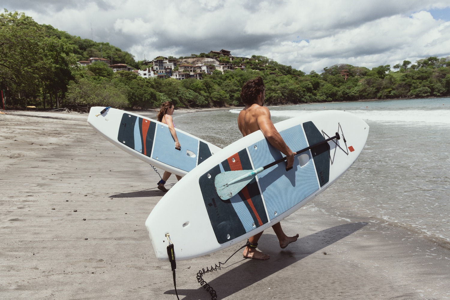 two people walking to the ocean holding paddle boards