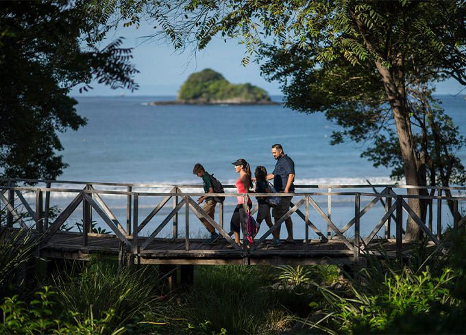 four people walking along a wooden bridge with the ocean in the background